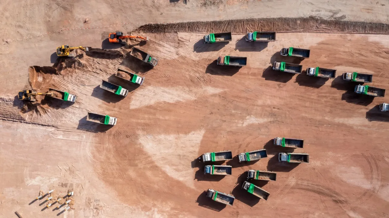 Excavators loading a fleet of trucks on a cleared plot, seen from directly above